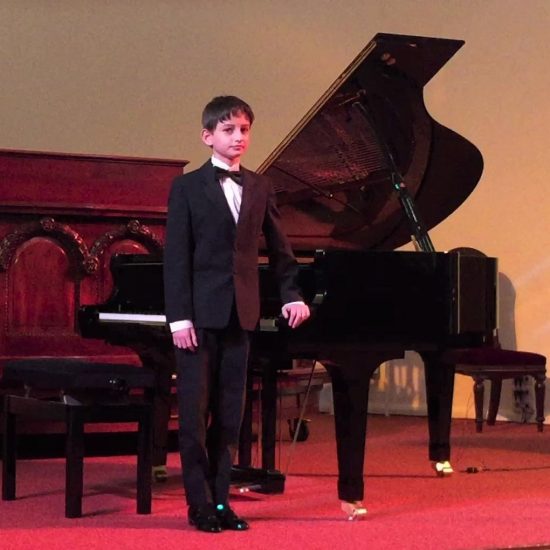 boy wearing a suit standing next to a grand piano