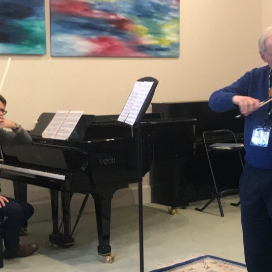 grey haired man playing violin with a girl playing violin and boy sitting at piano