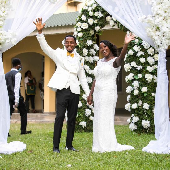 bride and groom under an arch waving